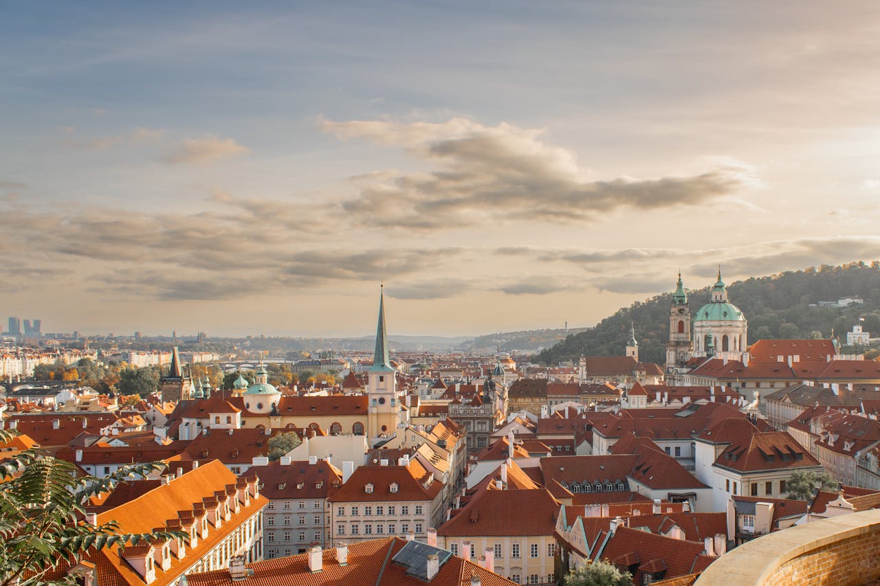 Captivating view of Prague's historic skyline with red rooftops and iconic architecture under a warm sunset.