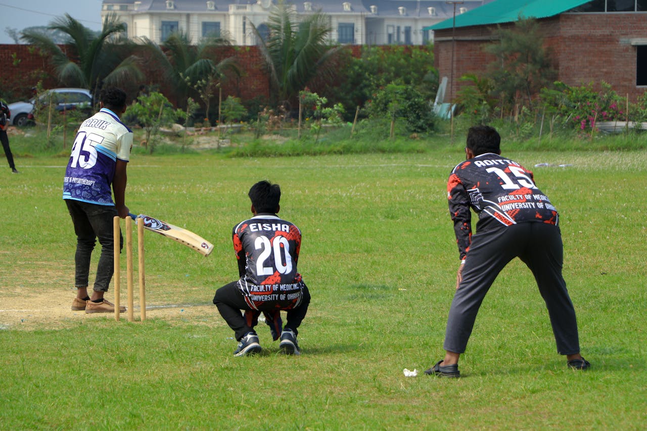 Cricket players in action on a sunny day at an outdoor field.